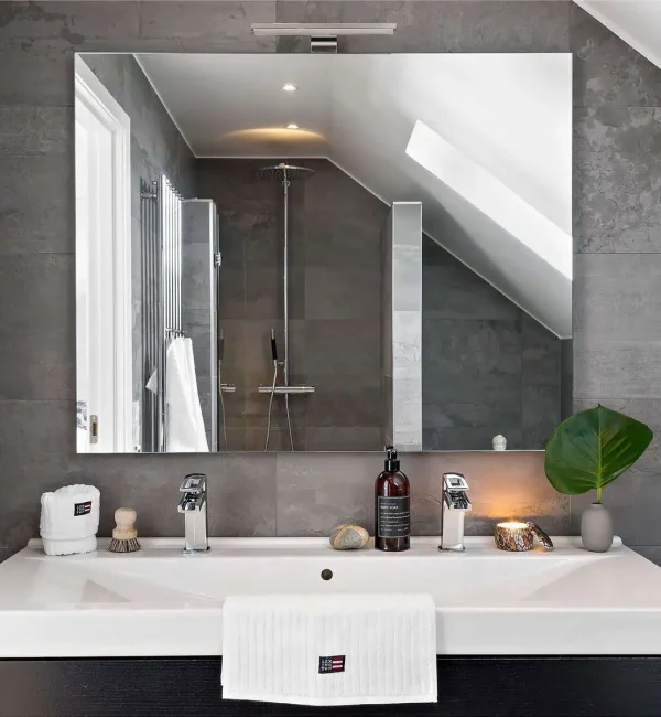 Totalrenovering i stockholm av badrum som har grått kakel, en stor spegel och stort handfat