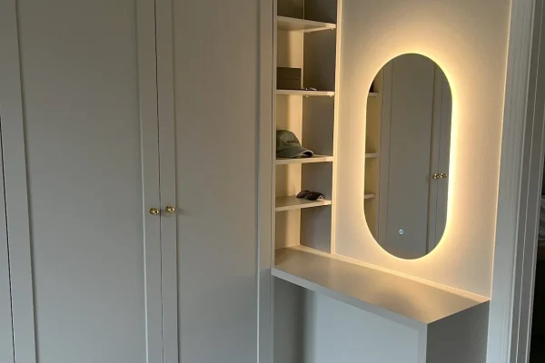 platsbyggda möbler i ett sovrum med ljusgrå garderob och ljusgrått sidorbord med en spegel ovanför
