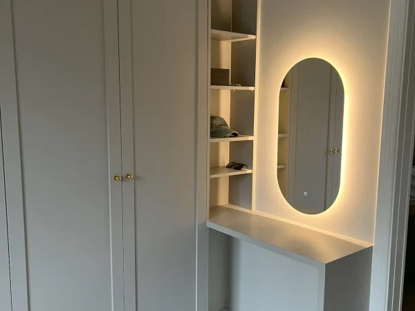 platsbyggda möbler i ett sovrum med ljusgrå garderob och ljusgrått sidorbord med en spegel ovanför